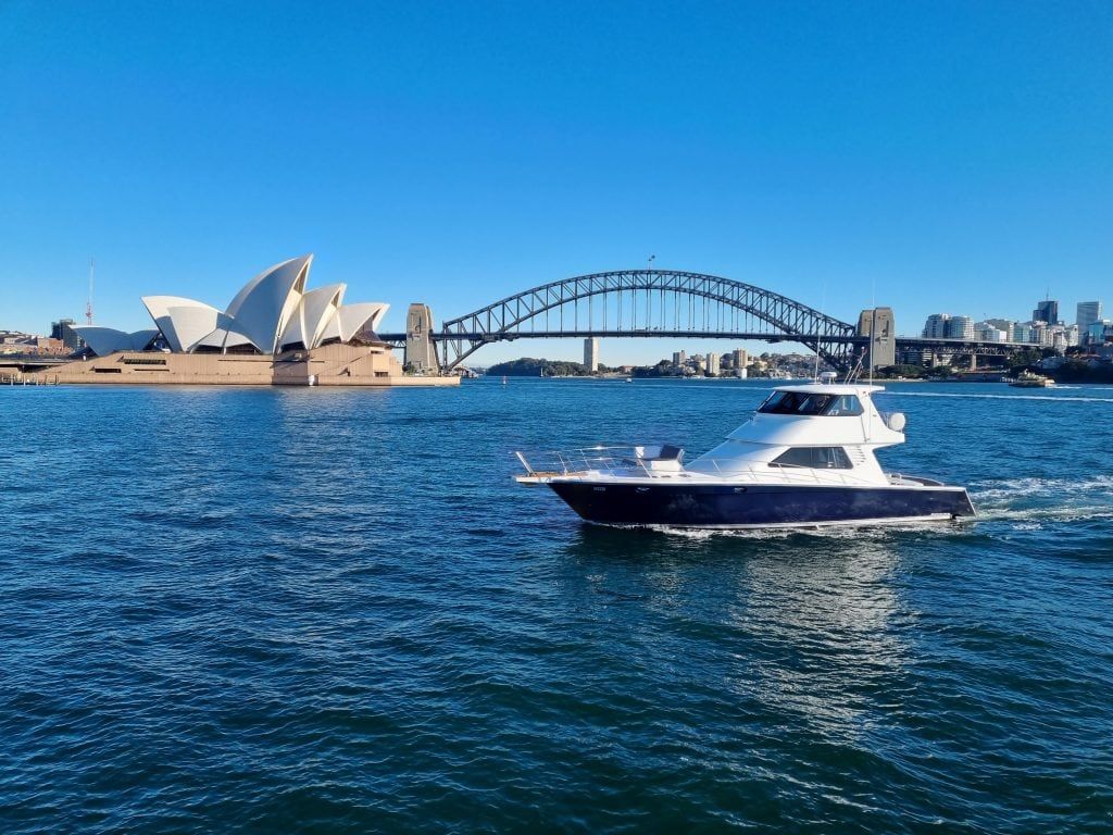 Commissioners steps circular quay: White and navy motor cruiser underway on harbour water with an opera house and steel arch