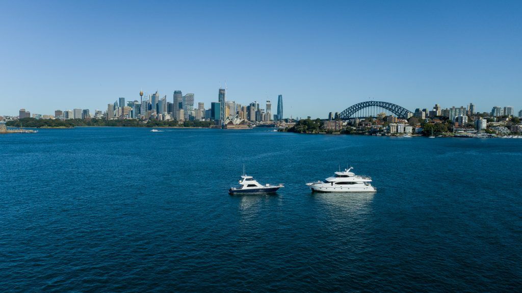 Pier 2: Two white motor yachts anchored on a wide harbour with a city skyline and arch bridge behind