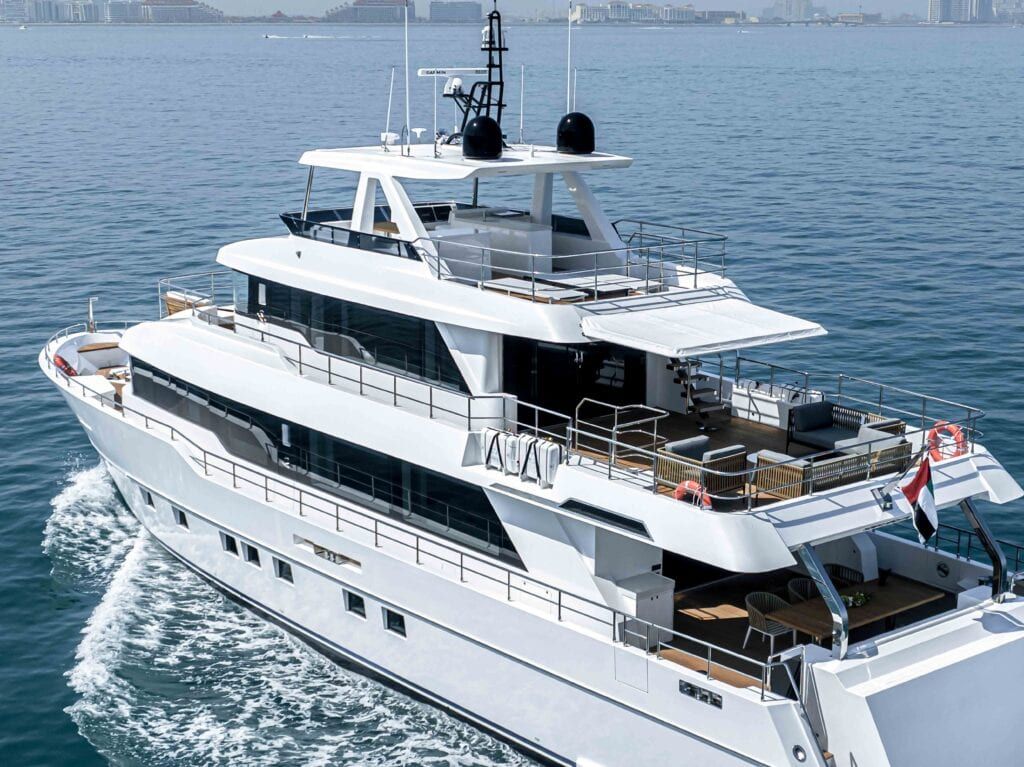 Boat hire: Aerial view of the white motor yacht Bluestone cruising on open water with a city skyline behind