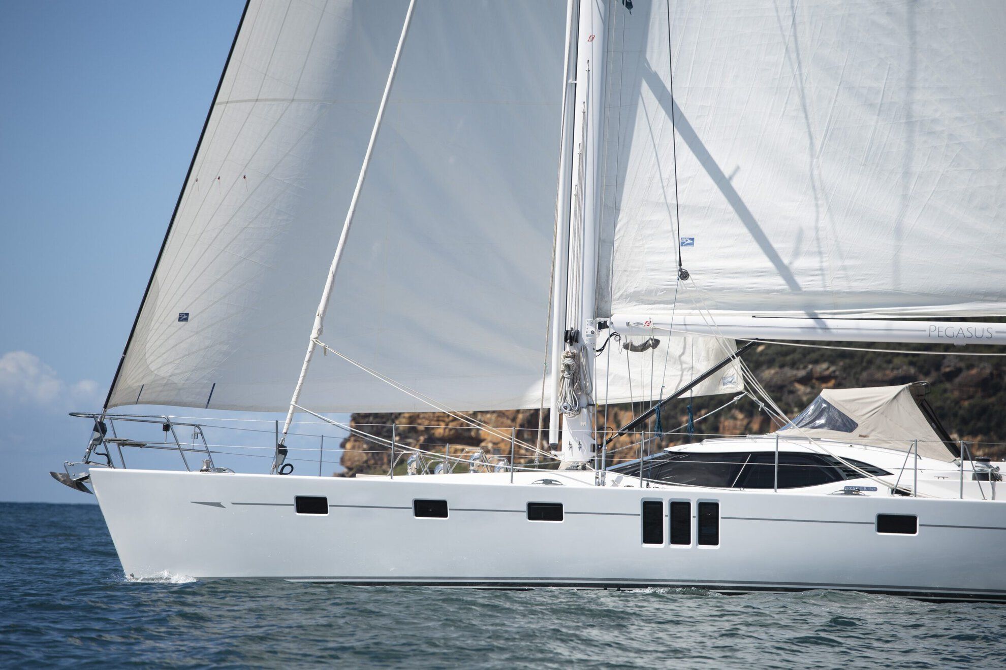 The sailing yacht Pegasus under full sail beside a rocky coastline