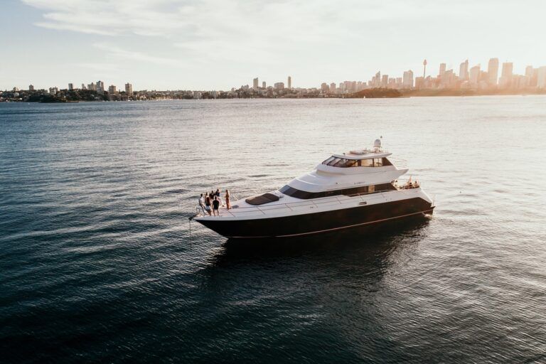 Aerial view of the motor yacht Element at anchor on open harbour water with a city skyline behind at sunset.