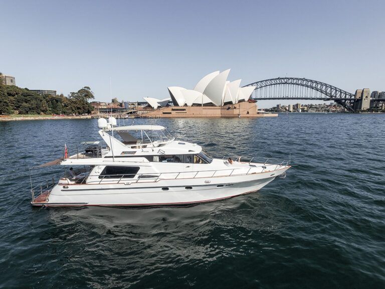 White motor yacht Enigma cruising on calm harbour water with the Sydney Opera House and Harbour Bridge behind.