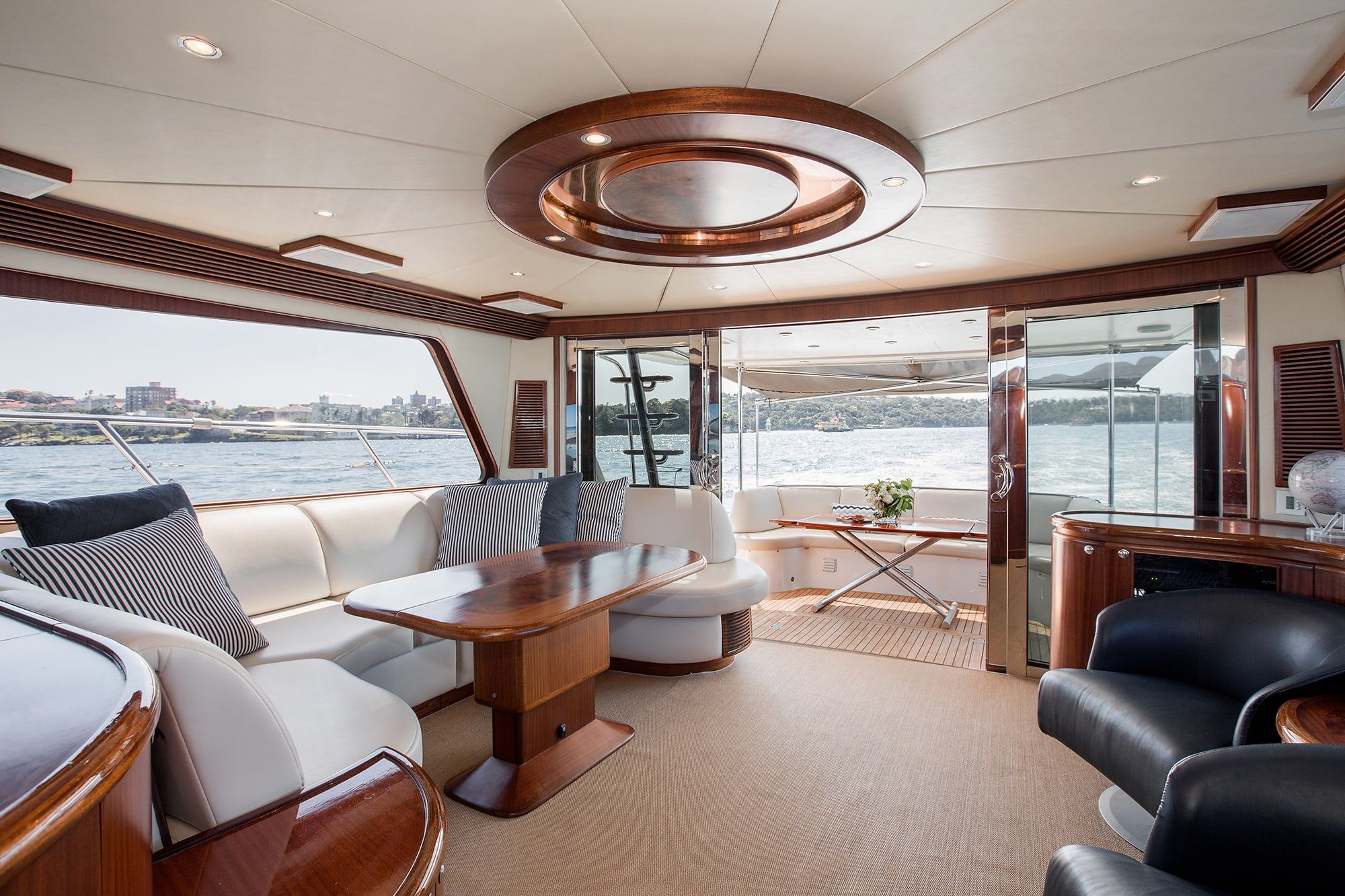Interior saloon of Enigma with white leather lounges, timber dining table and open doors to an aft deck over water.