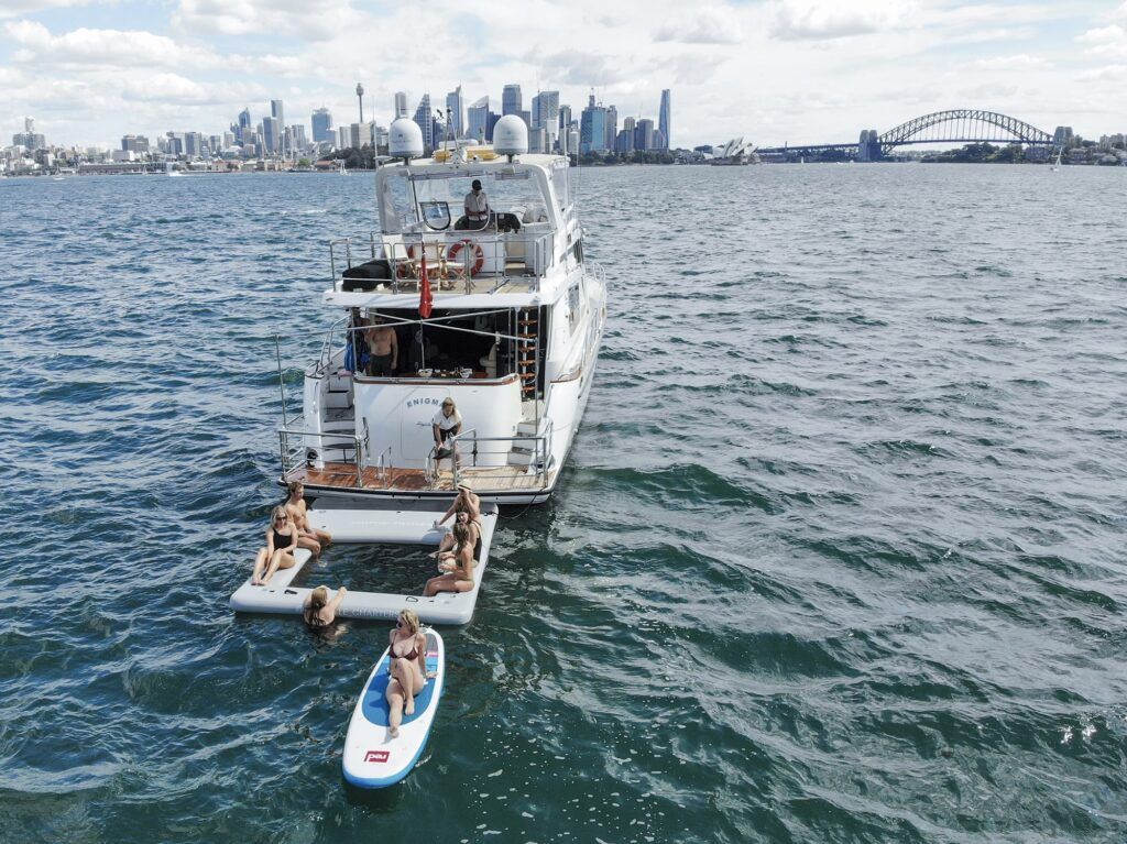 Bucks cruise sydney: Aerial view of a white motor yacht named Enigma with inflatable swim platforms and a paddleboard