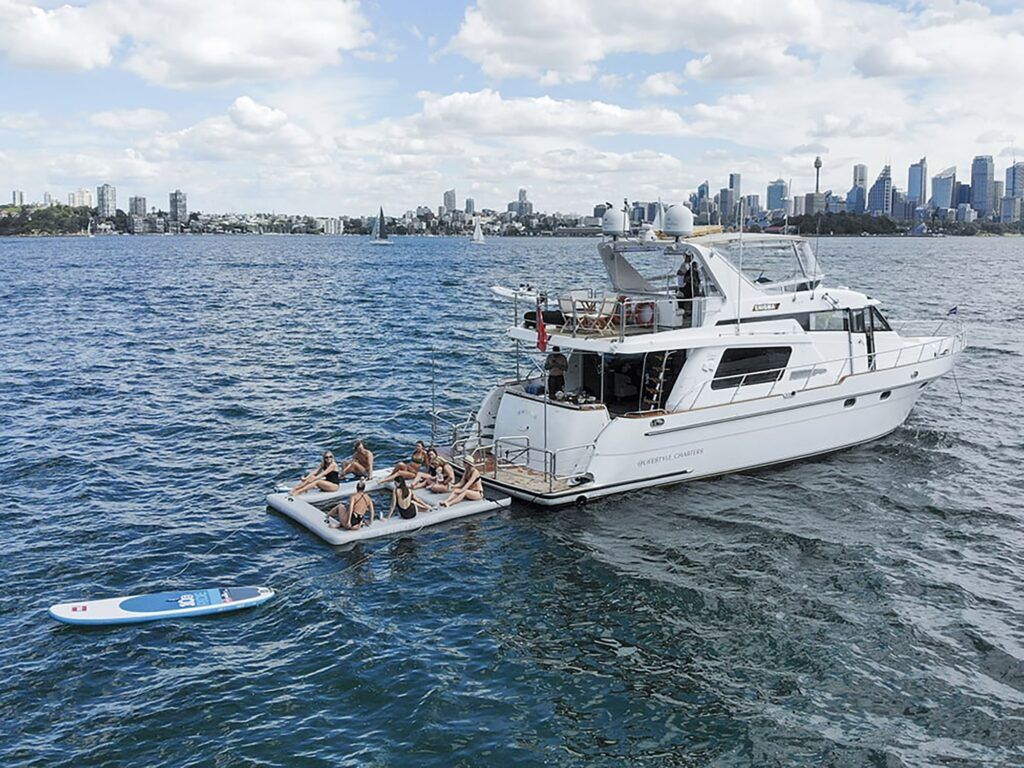 Harbour beach: Aerial view of the motor yacht Enigma anchored on a harbour with people sitting on an inflatable pontoon