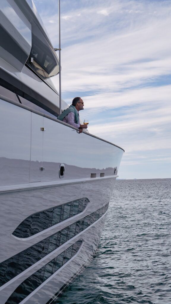 Manly boat rental: Man leaning on the railing of the motor yacht Mohasuwei with a glass of white wine, looking out to sea