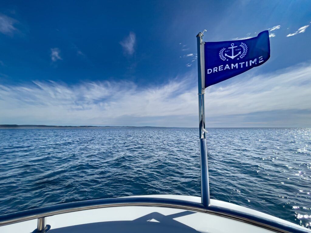 Double bay wharf: Blue flag with an anchor emblem and the word "Dreamtime" flying from a boat's bow rail over open water